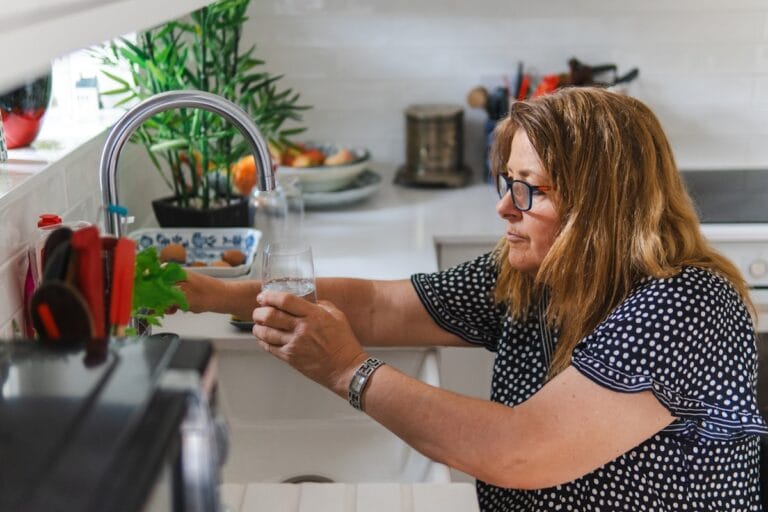 Mujer sirviendo agua pura del grifo en casa - sistema de ósmosis inversa Boom H2O